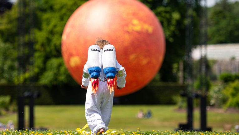 Child dressed as an astronaut runs in front of sculpture of Helios by Luke Jerram